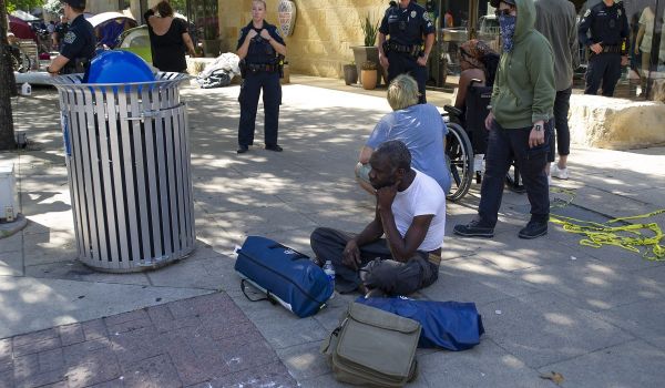 homeless man sitting near city hall as police watch the area