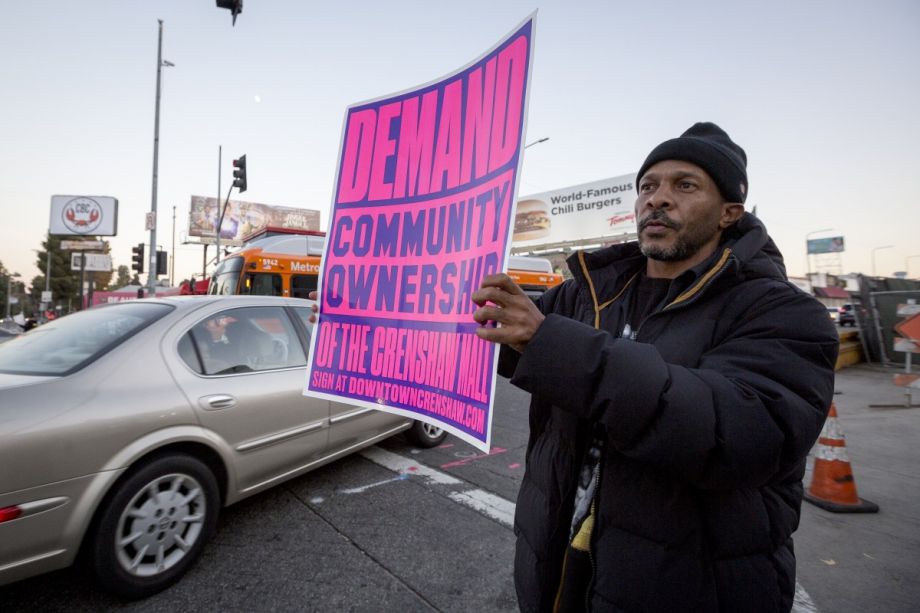 Activist Billion GODSun holds a sign demanding community ownership of the Baldwin Hills Crenshaw Plaza mall.
