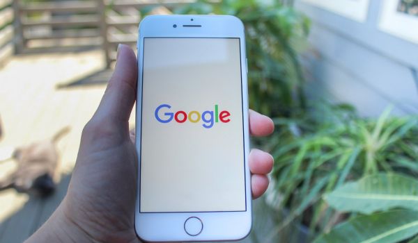 A hand holding a phone showing the Google logo