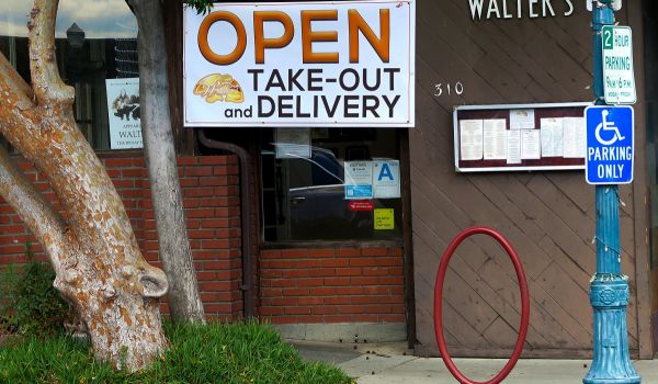 a restaurant with a sign saying it is open for takeout and delivery only, due to the covid-19 pandemic