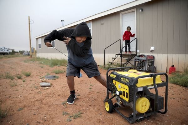 An Indigenous boy starts a generator outside his home.