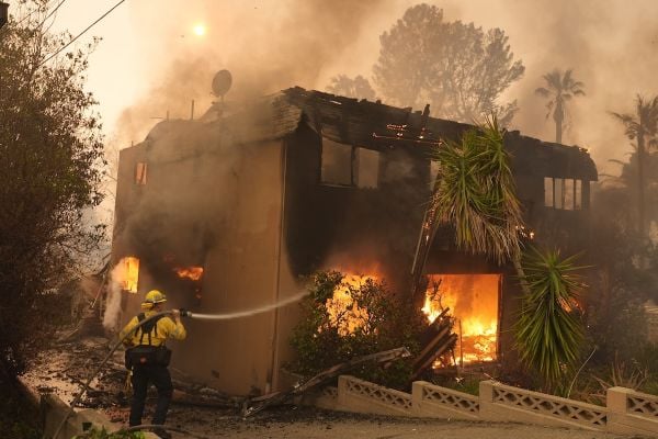 A firefighter tries to extinguish wildfire flames at a burning apartment building during the Eaton Fire, Jan. 8, 2025, in Altadena, California.