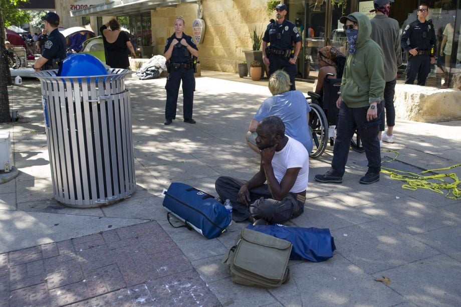 homeless man sitting near city hall as police watch the area