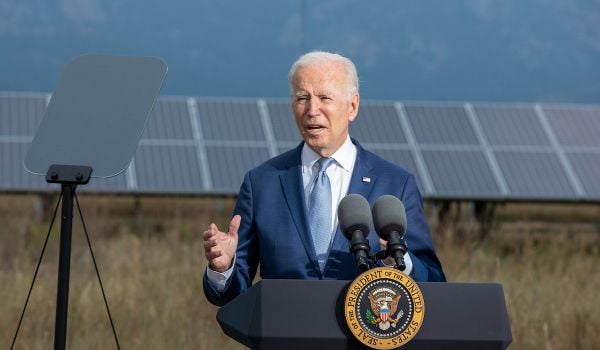 Joe Biden stands behind a podium with solar panels in background