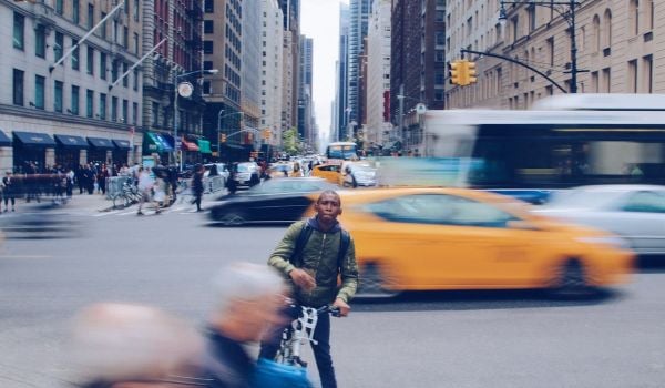 Black person on a bike with blurry cars and buses passing by them