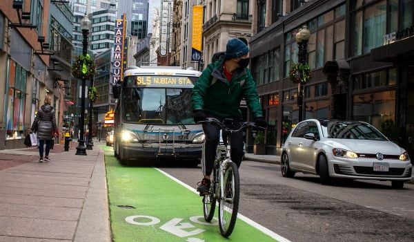 Biker rides in bike lane in front of public bus on a Boston street