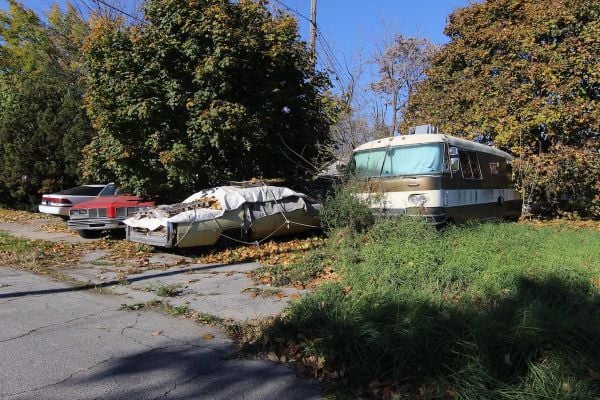 Abandoned cars parked on pavement and grass near trees in Detroit