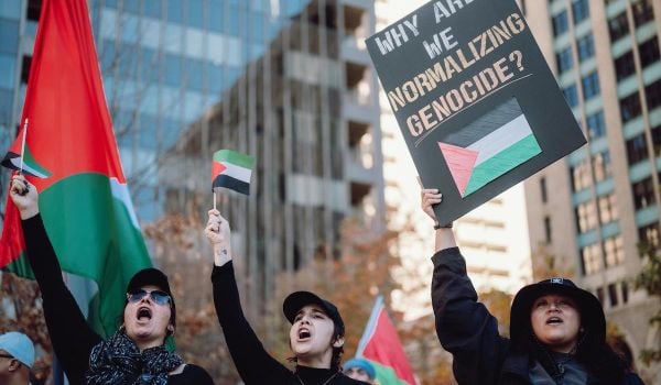 Three people with Palestinian flags and a banner at an antiwar Protest
