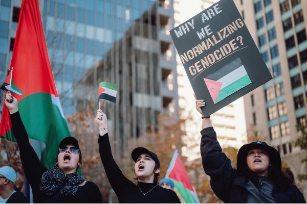 Three people with Palestinian flags and a banner at an antiwar Protest