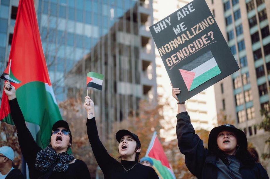 Three people with Palestinian flags and a banner at an antiwar Protest
