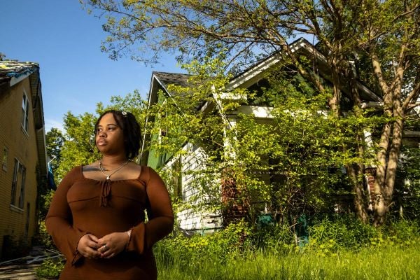 Person on left side of image, with a home and trees in the background