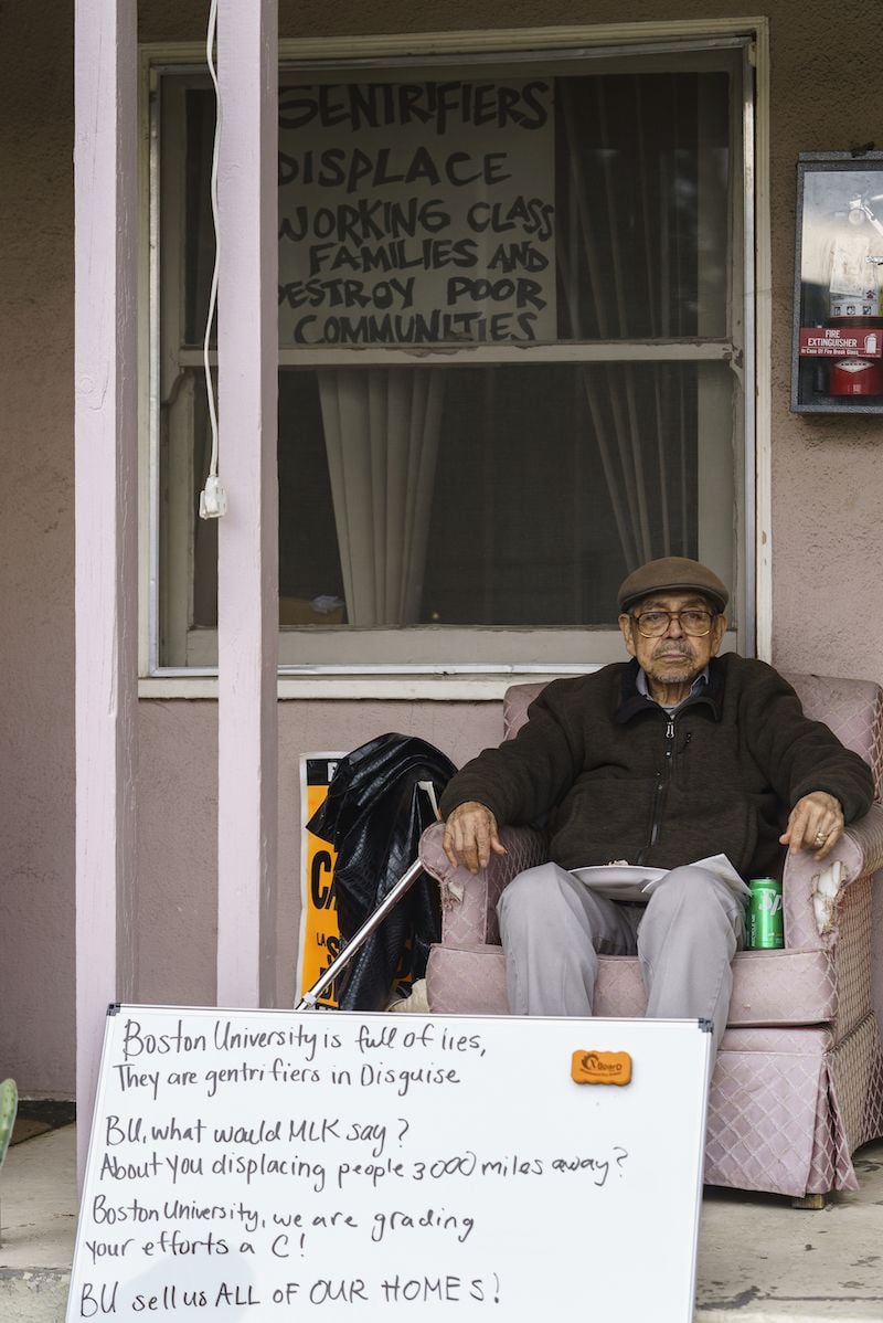 Jorge Lopez sits on the porch in front of his home, with protest signs