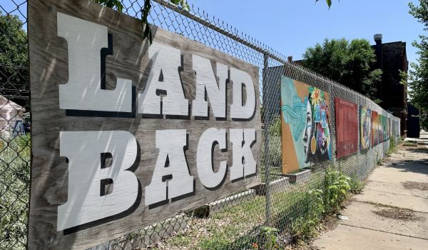 Mural that reads 'Land Back' with Indigenous artwork along fence