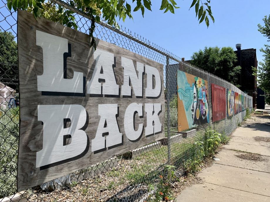 Mural that reads 'Land Back' with Indigenous artwork along fence