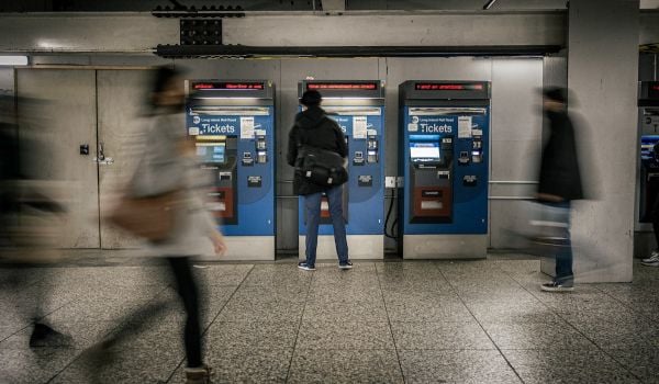 Person buys ticket at Metrocard kiosk; other people are blurred walking behind them