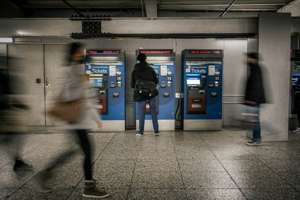 Person buys ticket at Metrocard kiosk; other people are blurred walking behind them