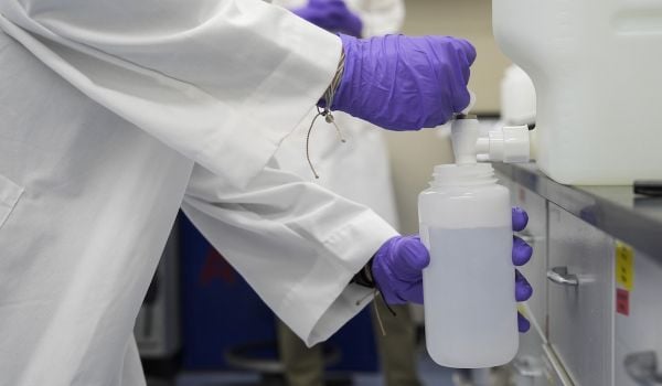 Person wearing purple gloves pours water sample into a smaller container.