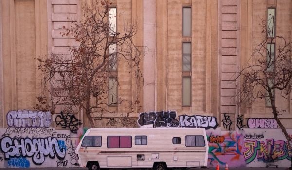 RV parked on a street with wall tagged with graffiti in the background