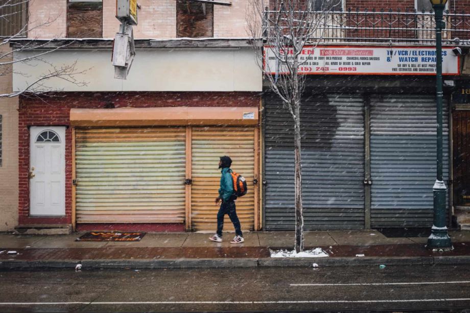 Person walks down a street in Philadelphia; there are flurries of snow in the air and on the ground