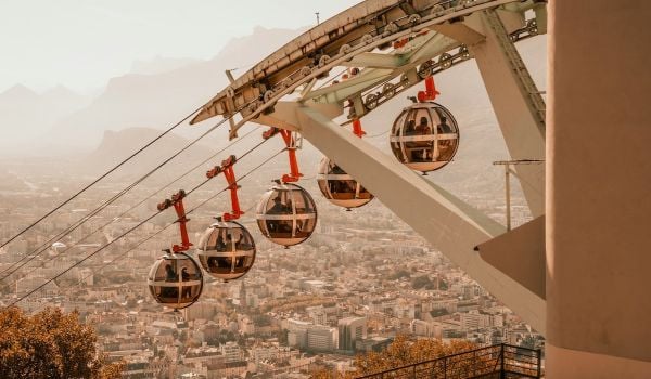 Four aerial cable cars make their way down; buildings in city can be seen in background