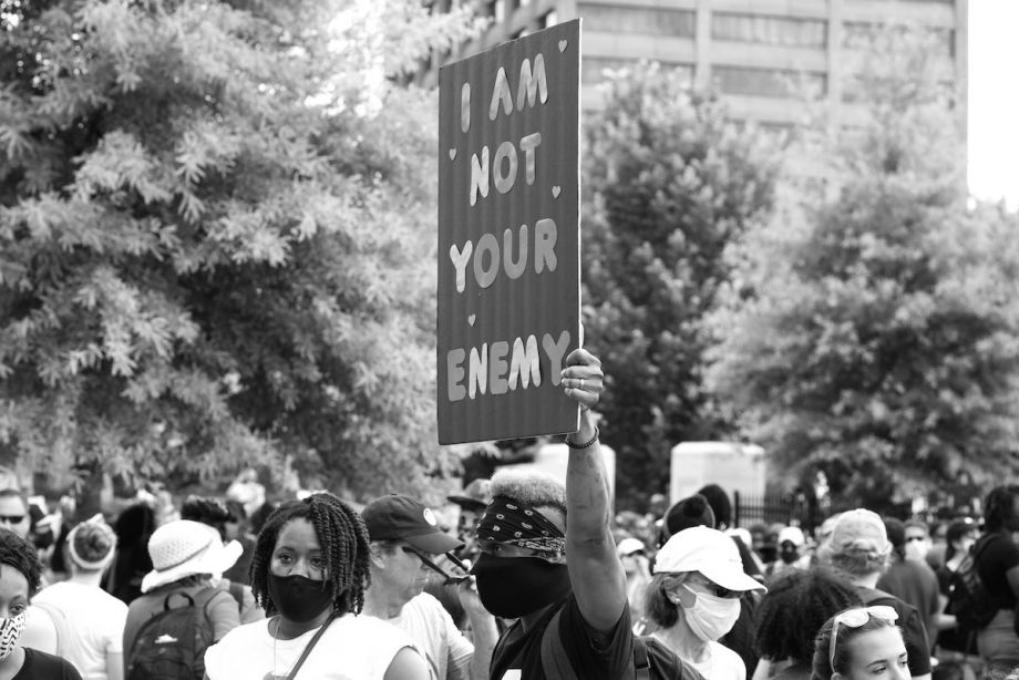 In a crowd at a protest, person holds a sign that reads 'I'm not your enemy'