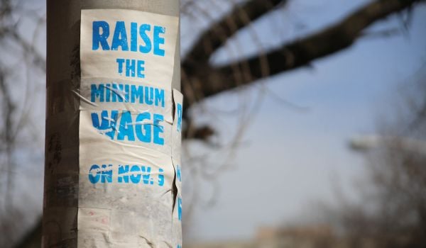 White paper taped to pole that reads, 'Raise the Minimum Wage on Nov. 5' in blue writing